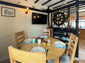 A dining area with a round wooden table, chairs, and a television mounted on the wall. - 2 bedroom accommodation in Whitby (Whitby)