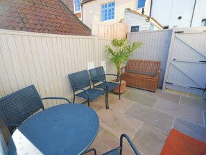 Un espace patio comprenant une table ronde, deux chaises, un banc et un pot de fleurs.