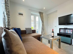 A living room with a sofa, a coffee table, a TV, and a bookshelf. - 2 bedroom accommodation in Whitby (Whitby)