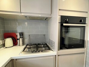 Une cuisine équipée d’une cuisinière à gaz, d’un four et d’une bouilloire rouge pos ée sur le plan de travail.
