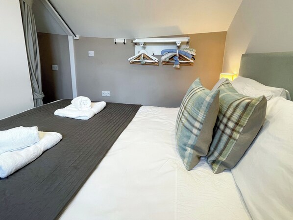 Une chambre d’hôtel comprenant un lit, une table de chevet, un porte-vêtements et une prise électrique murale.