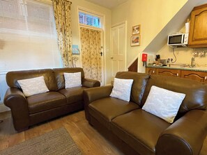 Ein Wohnzimmer mit zwei braunen Ledersofas, Holzboden und einer Küchenzeile inklusive Mikrowelle.