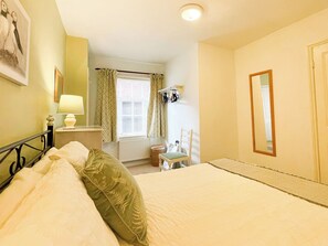 A hotel room with a bed, a bedside table with a lamp, a chair, a window with curtains, a radiator, and a mirror on the wall. - 2 bedroom accommodation in Whitby (Whitby)