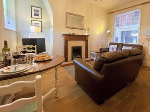 A living room with a fireplace, a brown leather sofa, a dining table with a plate of food, and a television. - 2 bedroom accommodation in Whitby (Whitby)