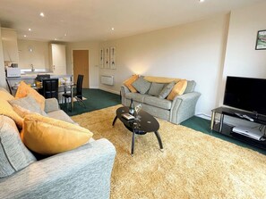Ein Wohnzimmer mit grauem Sofa, einem Couchtisch und einem Fernseher.