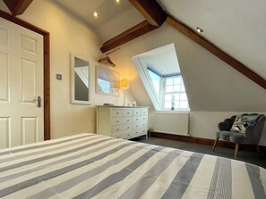A bedroom with a sloped ceiling, a bed with striped bedding, a dresser, a chair, and a window with a view. - 2 bedroom accommodation in Whitby (Whitby)