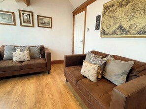A room with two brown leather sofas, wooden flooring, and a large world map on the wall. - 2 bedroom accommodation in Whitby (Whitby)