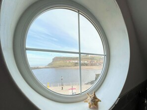 A window with a view of a coastal town, a body of water, and a distant hill with buildings. - 2 bedroom accommodation in Whitby (Whitby)