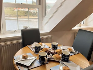 A dining table with a view of a body of water and buildings, equipped with chairs, plates of scones, and coffee mugs. - 2 bedroom accommodation in Whitby (Whitby)