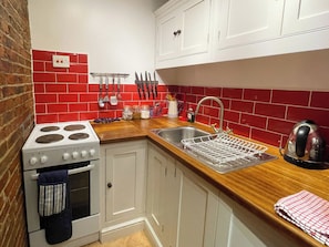 A kitchen with a stove, sink, and red-tiled backsplash. - 3 bedroom accommodation in Whitby (Whitby)