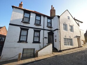A two-story building with a white facade and black window frames, featuring a small entrance and a staircase leading to the ground floor. - 3 bedroom accommodation in Whitby (Whitby)