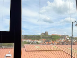 En vy över en stad med ett ståtligt slott på en kulle, en fågel på ett hustak och en klar himmel.