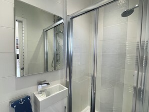 A modern bathroom with a glass-enclosed shower, a white sink with a mirror above it, and a towel rack with a blue towel. - 3 bedroom accommodation in Whitby (Whitby)
