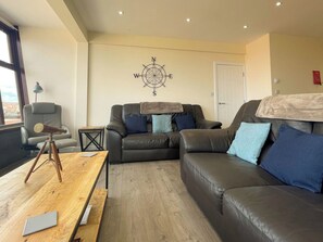 A modern living room with a leather sofa, a wooden coffee table, and a compass wall decoration. - 3 bedroom accommodation in Whitby (Whitby)