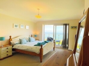 A bedroom with a bed, bedside tables, a lamp, and a view of the sea through a sliding door. - 1 bedroom accommodation in Whitby (Whitby)