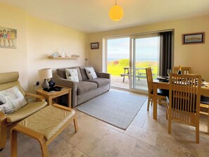 A living room with a sofa, a chair, a table, and a view of the outdoors through a sliding glass door. - 1 bedroom accommodation in Whitby (Whitby)