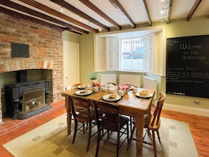 A dining area with a brick fireplace, wooden table, and chairs. There is a window with white shutters and a chalkboard with a welcome message. - 3 bedroom accommodation in Whitby (Whitby)