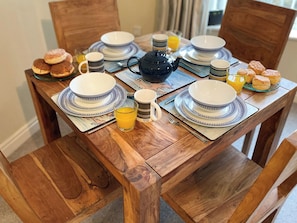A wooden dining table set with plates, bowls, a teapot, cups, and a glass of orange juice. - 2 bedroom accommodation in Whitby (Whitby)