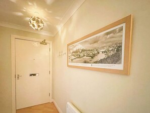 A hallway with a white door, a framed black and white photograph on the wall, and a ceiling light fixture. - 2 bedroom accommodation in Whitby (Whitby)