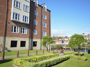 A multi-story residential building with a brick facade, multiple windows, and a landscaped garden with flowers and trees. - 2 bedroom accommodation in Whitby (Whitby)