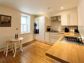 A compact kitchen with a wooden countertop, white cabinets, a built-in oven, and a window with blinds. - 3 bedroom accommodation in Whitby (Whitby)