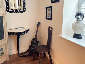 A room with a wooden guitar leaning against a wall, a decorative chair, and a shelf with a bust. - 3 bedroom accommodation in Whitby (Whitby)