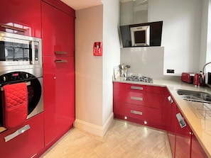 A modern kitchen with red cabinetry, stainless steel appliances, and a built-in microwave. - 1 bedroom accommodation in Whitby (Whitby)