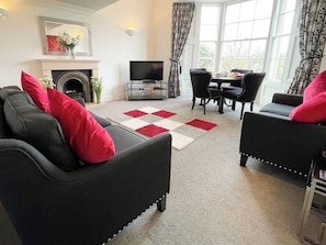 A living room with a fireplace, a television, and a dining area with chairs and a table. - 1 bedroom accommodation in Whitby (Whitby)