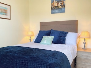 A neatly made bed with a blue blanket and pillows, two bedside lamps, and a framed picture on the wall. - 1 bedroom accommodation in Whitby (Whitby)
