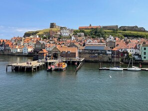 A coastal town with a historic castle on a hill, a dock with boats, and a variety of buildings with red roofs. - 1 bedroom accommodation in Whitby (Whitby)