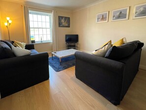 A living room with two sofas, a coffee table, a TV, and a window with curtains. - 2 bedroom accommodation in Whitby (Whitby)
