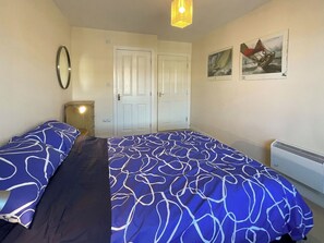 A bedroom with two beds, a dresser, a mirror, a door, and a wall-mounted heater. - 2 bedroom accommodation in Whitby (Whitby)
