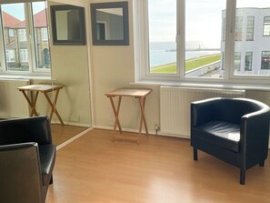 Habitació amb vista al mar, una cadira negra, dues taules de fusta i un radiador.