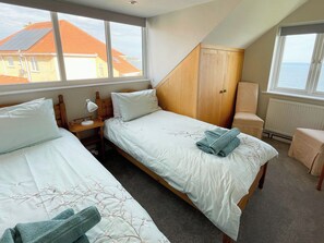 A bedroom with two beds, a wooden wardrobe, a chair, and a view of the sea. - 3 bedroom accommodation in Whitby (Whitby)
