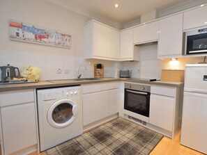 A compact kitchen with a washing machine, oven, microwave, and a plaid rug. - 2 bedroom accommodation in Whitby (Whitby)