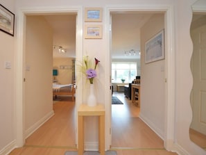 A hallway with a bed, a dining area, and a small table with a vase of flowers. - 2 bedroom accommodation in Whitby (Whitby)