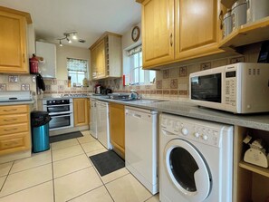 A kitchen with wooden cabinets, a microwave, a washing machine, and a stove. - 2 bedroom accommodation in Whitby (Whitby)