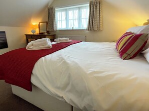 A neatly made bed with white linens and a red blanket, a bedside table with a lamp, a window with curtains, and a wall-mounted mirror. - 2 bedroom accommodation in Whitby (Whitby)