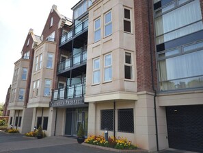 Un edificio de varios pisos con un letrero que dice 'Caedmons Prospect'. Presenta un diseño arquitectónico moderno con una combinación de paredes exteriores de ladrillo y color beige, ventanas amplias y un balcón en el segundo piso.
