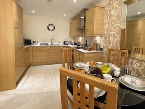 A modern kitchen with wooden cabinets, a central island, and a dining area with a table set for breakfast. - 2 bedroom accommodation in Whitby (Whitby)