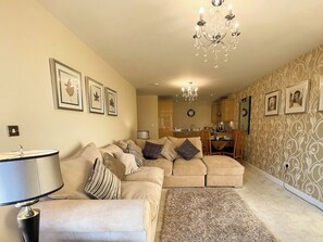 A living room with a sofa, a lamp, a chandelier, and framed pictures on the wall. - 2 bedroom accommodation in Whitby (Whitby)