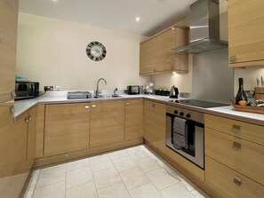 A modern kitchen with wooden cabinets, a stainless steel sink, a built-in oven, and a wall-mounted clock. - 2 bedroom accommodation in Whitby (Whitby)