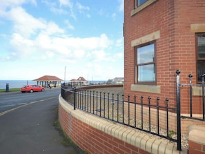 A coastal building with a brick facade, a black metal fence, and a red car parked on the adjacent road. - 2 bedroom accommodation in Whitby (Whitby)