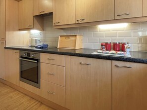 A kitchen with wooden cabinets, a built-in oven, and a countertop with various items including a cutting board, jars, and a coffee maker. - 2 bedroom accommodation in Whitby (Whitby)