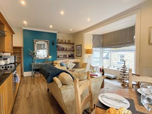 A cozy living room with a sofa, a dining table set for two, and a kitchen area with a stove and cabinets. - County Retreat Apartment (Whitby)
