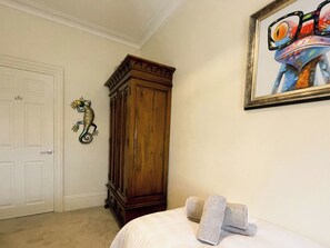 A bedroom with a wooden wardrobe, a door, a painting, and towels on the bed. - County Retreat Apartment (Whitby)
