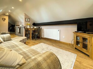 A cozy living room with a sofa, a dining table with chairs, a kitchen area with an oven, and a television on a wooden cabinet. - 1 bedroom accommodation in Whitby (Whitby)