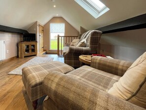 A cozy living room with a high ceiling, a wooden cabinet, a television, and a view of the outdoors through a window. - 1 bedroom accommodation in Whitby (Whitby)