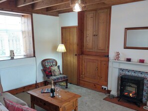 A cozy room with a wooden floor, a fireplace, a wooden cabinet, a plaid chair, a table with a bottle and glasses, and a window with blinds. - 3 bedroom accommodation in Fylingthorpe (Fylingthorpe)