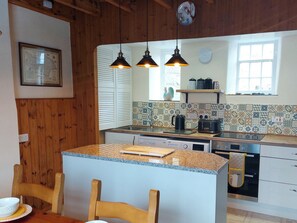A kitchen with wooden cabinets, a granite countertop, a dining area with a table and chairs, pendant lights, and a window with a view. - 3 bedroom accommodation in Fylingthorpe (Fylingthorpe)
